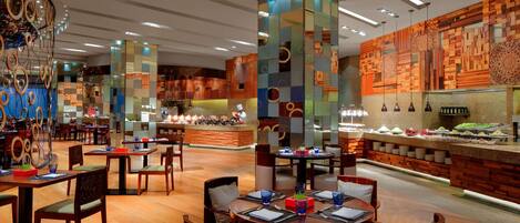A modern restaurant with wooden flooring, round tables, and chairs. There are decorative pillars and a wall with a geometric pattern.