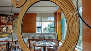 A modern dining area with round tables and white chairs, large windows, and a decorative mirror. - Radisson Blu Cebu (Cebu City)