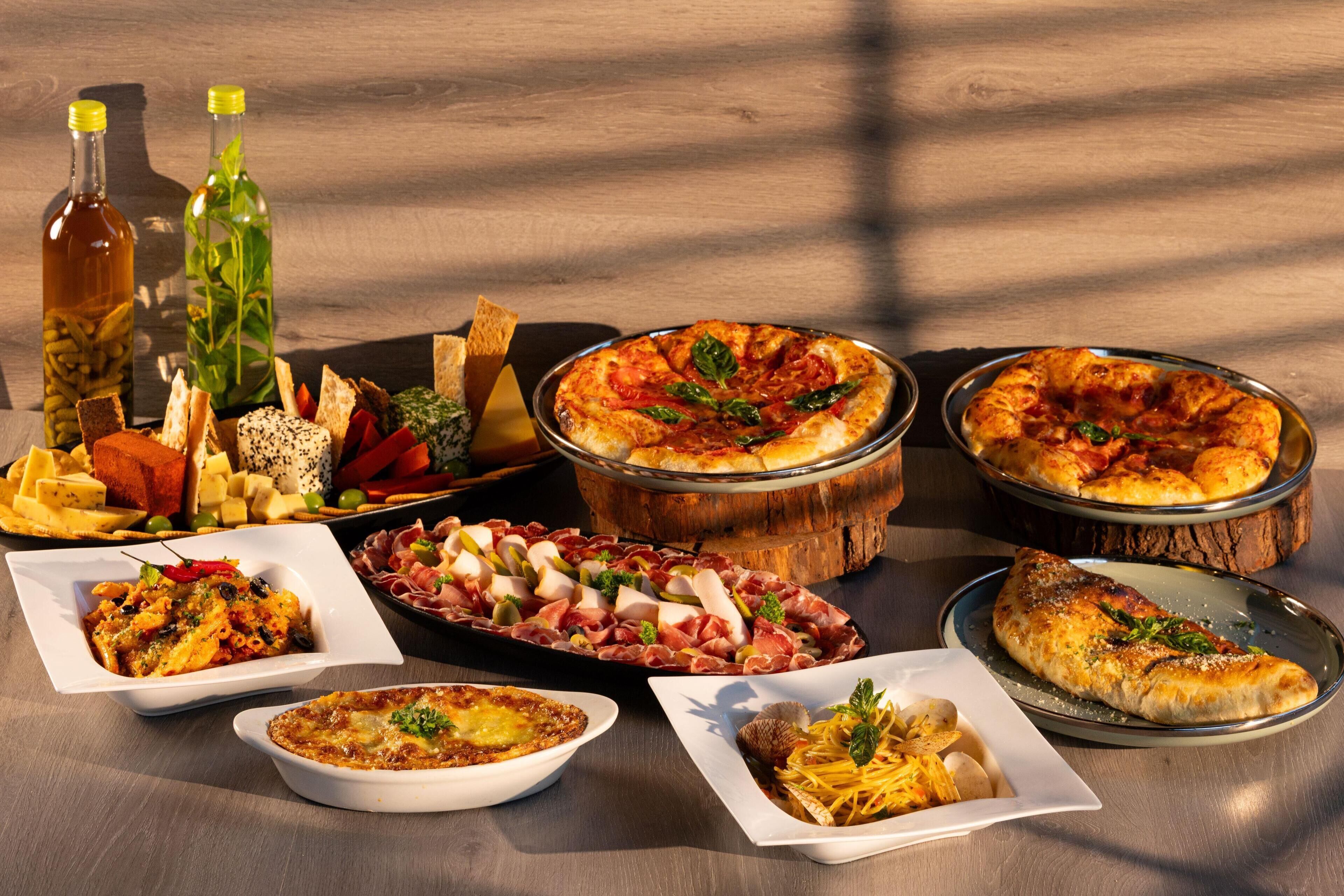 A variety of dishes including pizza, pasta, and charcuterie on a wooden table.