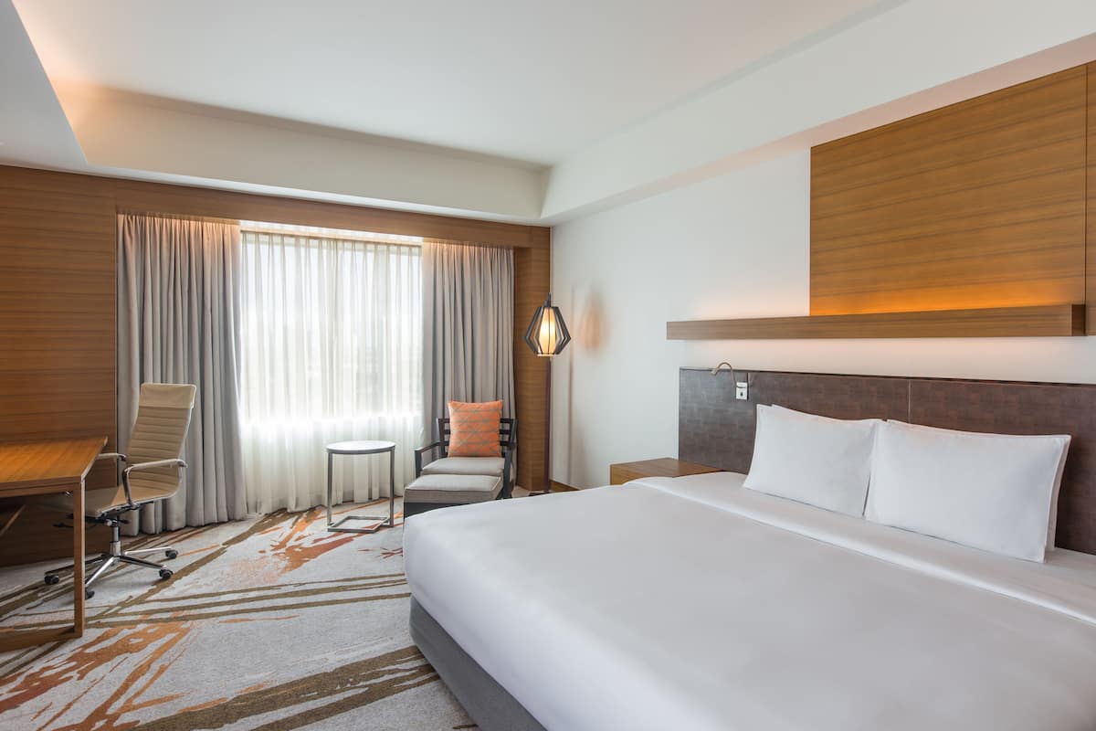 A hotel room with a large bed, a desk with a chair, a small table, and a lamp.