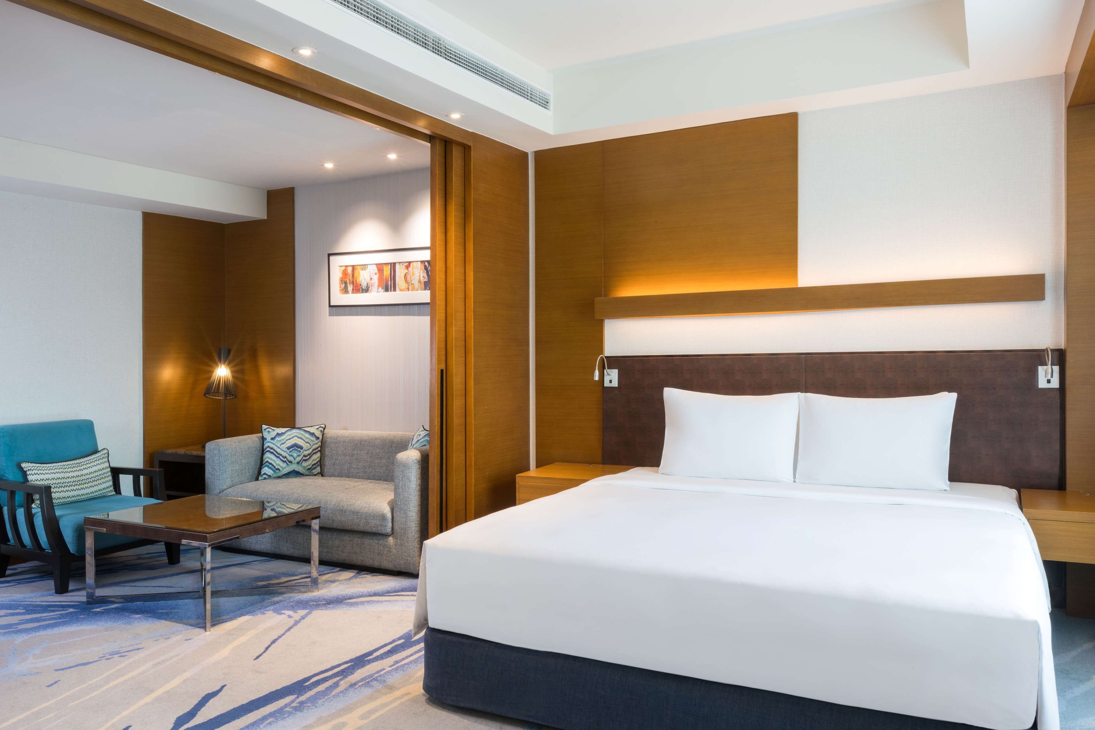 A modern hotel room with a large bed, a sofa, a coffee table, and a wall-mounted TV.