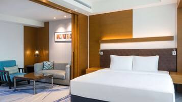 Una habitación de hotel moderna con una cama grande, un sofá, una mesa de centro y un televisor instalado en la pared.