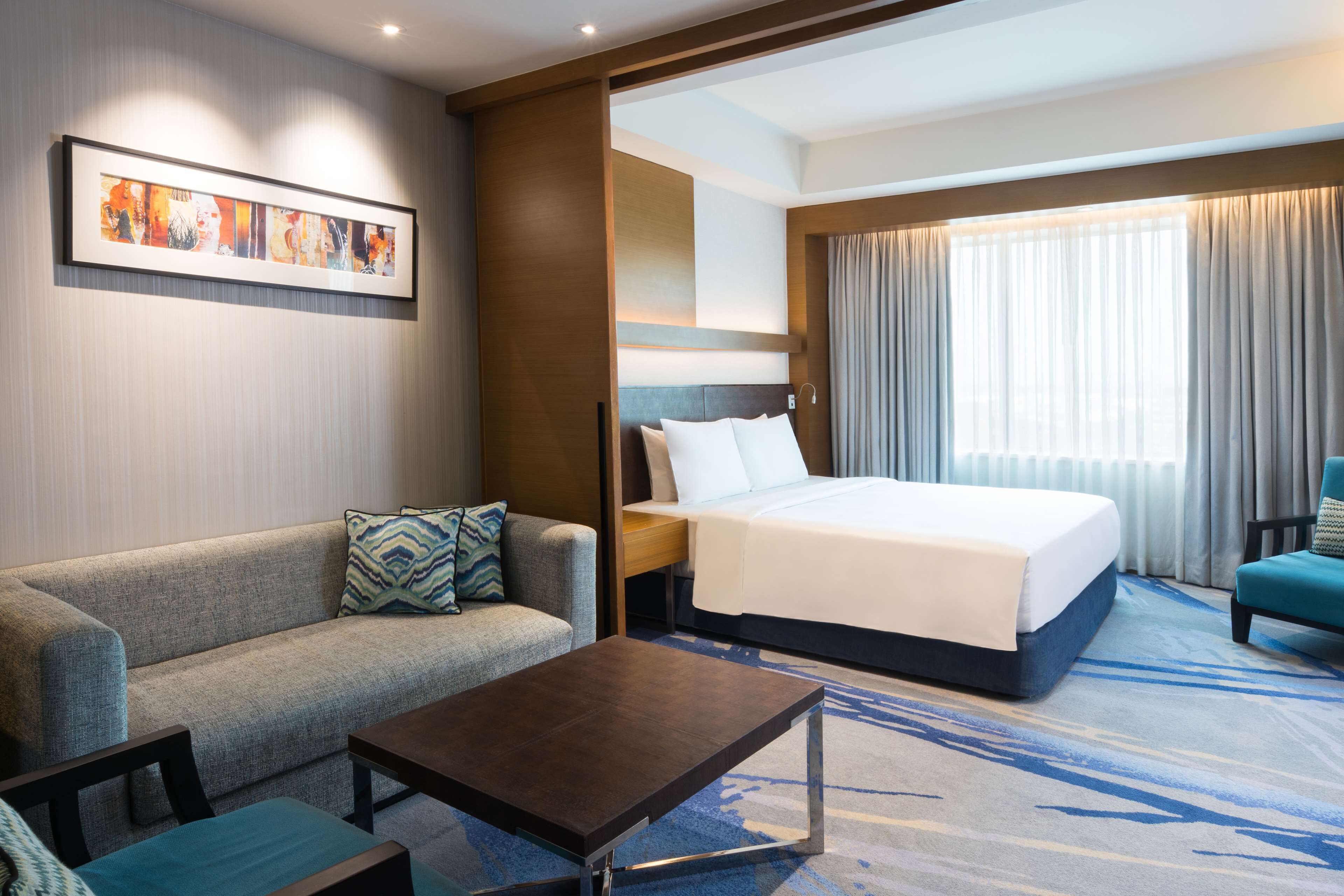 Una habitación de hotel con cama, sofá, mesa de centro y un cuadro en la pared.