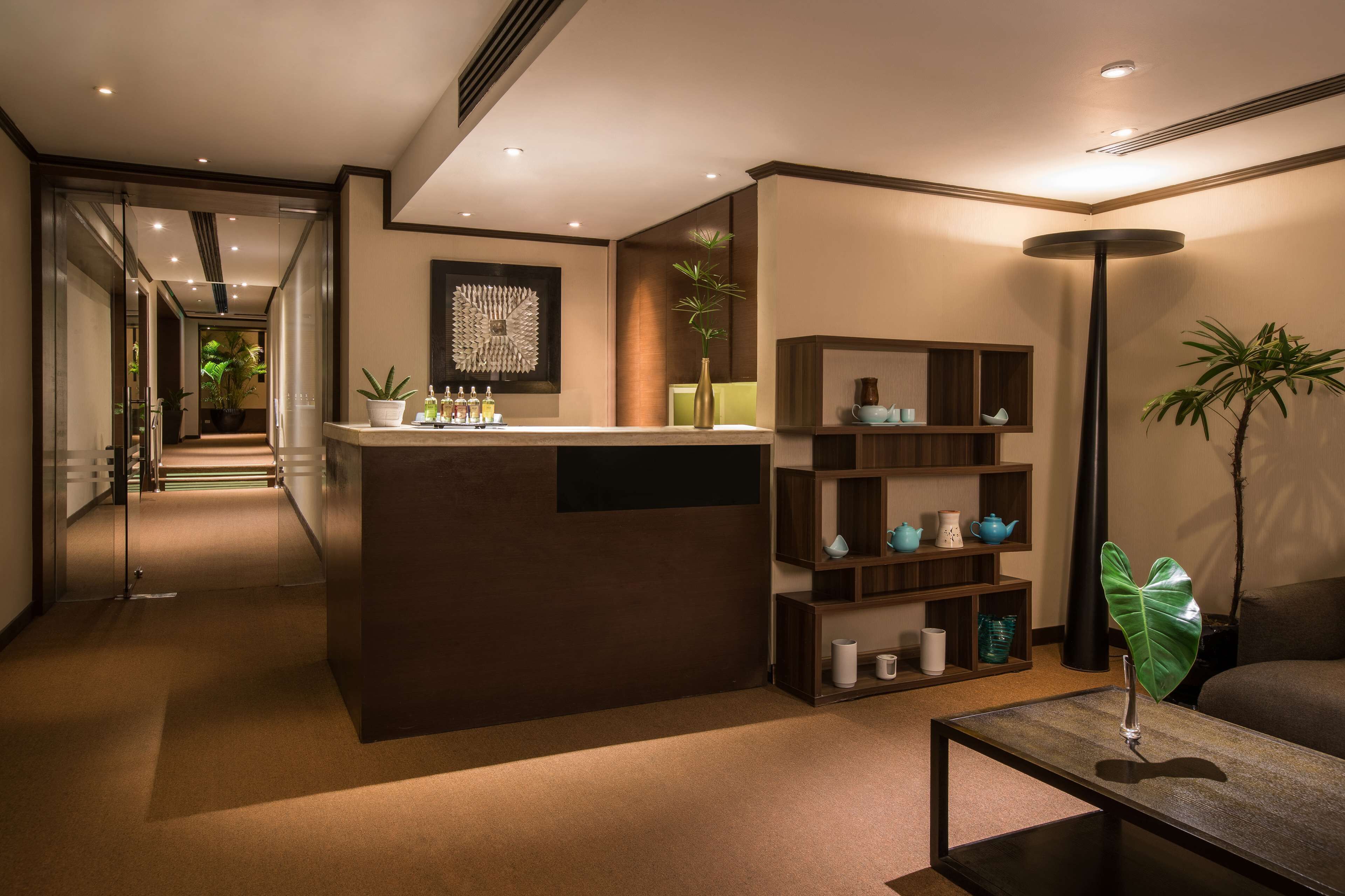 A modern lobby with a reception desk, a coffee machine, a potted plant, and a bookshelf.