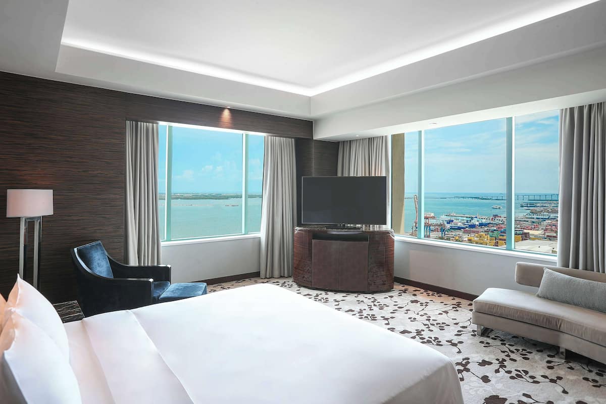 A hotel room with a large bed, a sofa, a TV, and a view of the sea.