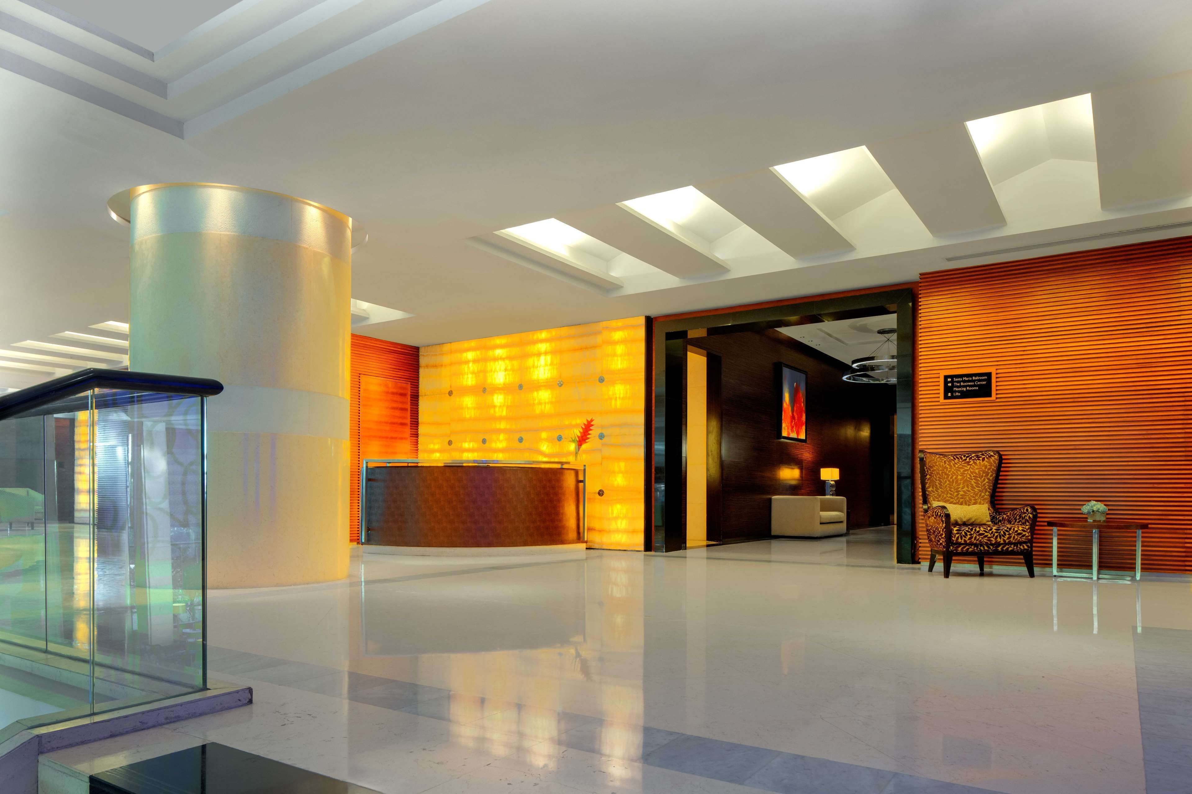 A modern lobby with a reception desk, a seating area with a patterned chair, and a glass partition.