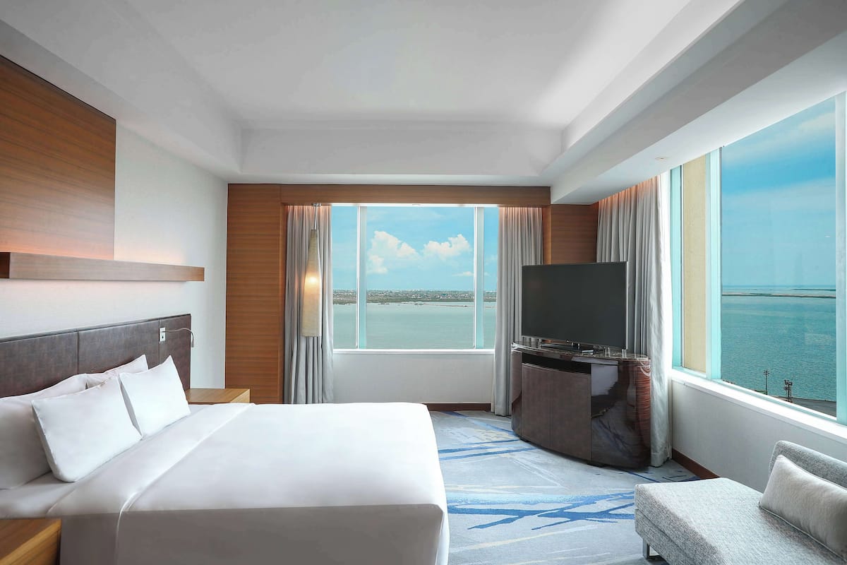 A hotel room with a large bed, a TV, a desk, and a view of the sea.