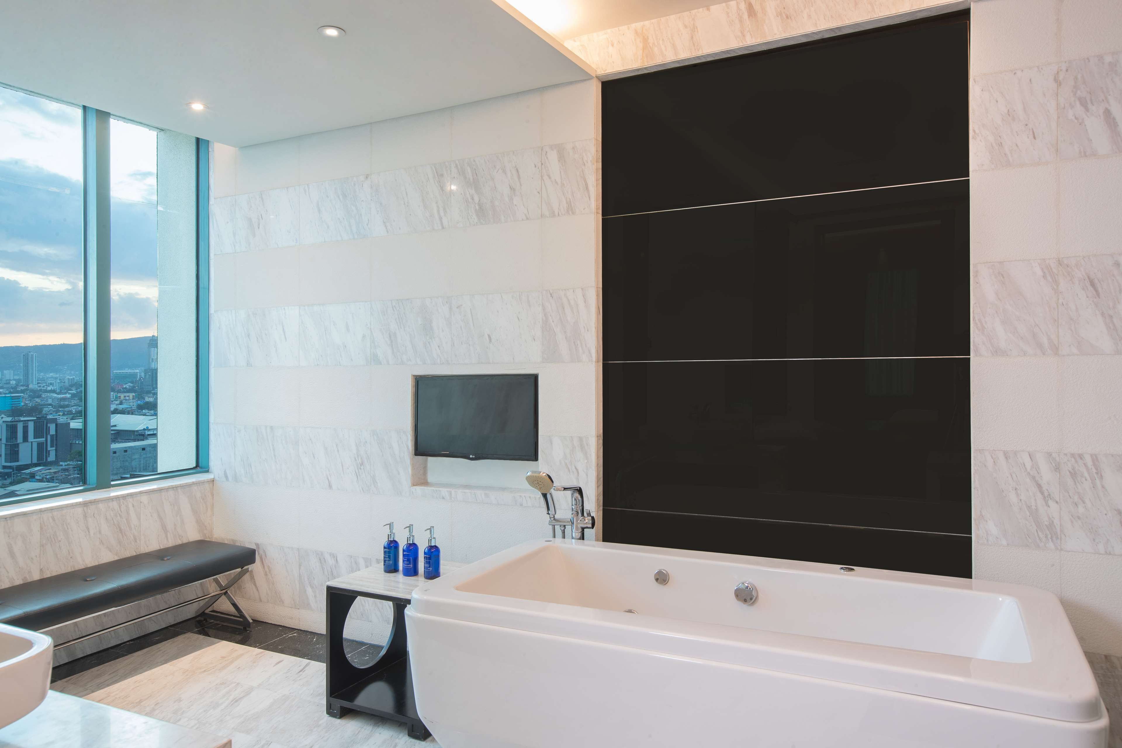 A modern bathroom with a large bathtub, a bench, and a view of the city through large windows.