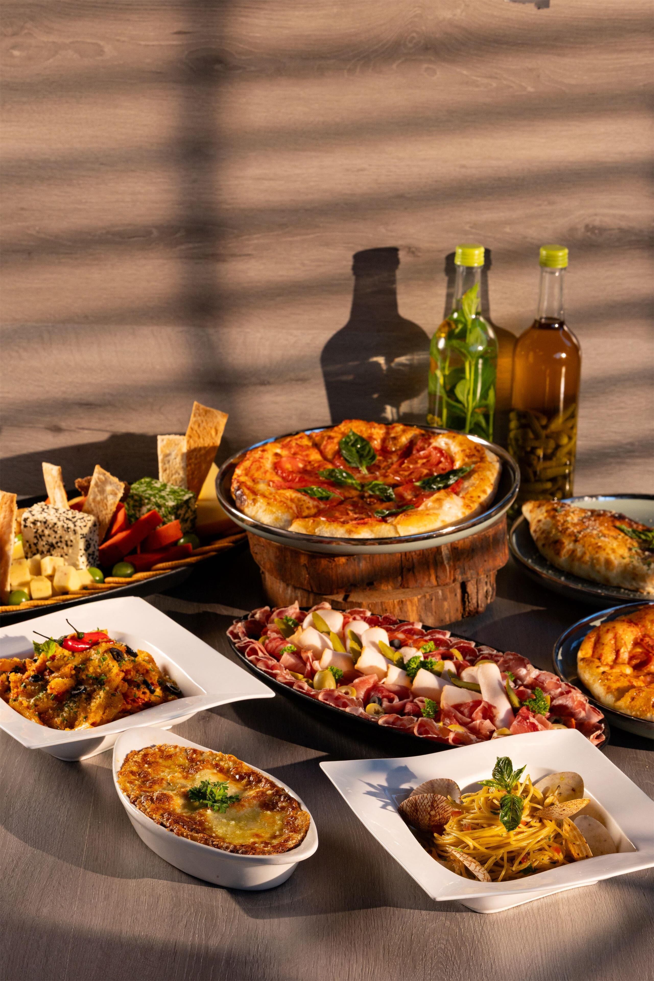 A variety of dishes including pizza, pasta, and cheese platters on a wooden table.