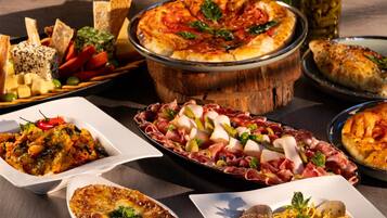 A variety of dishes including pizza, pasta, and cheese platters on a wooden table.