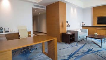 Una habitación de hotel moderna con un escritorio de madera, un sofá, un televisor montado en la pared y una alfombra estampada.