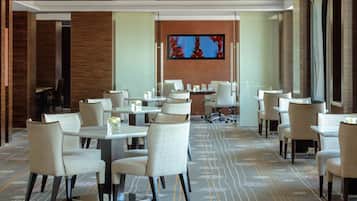 A conference room with multiple tables and chairs, a large flat-screen TV on the wall, and a patterned carpet.