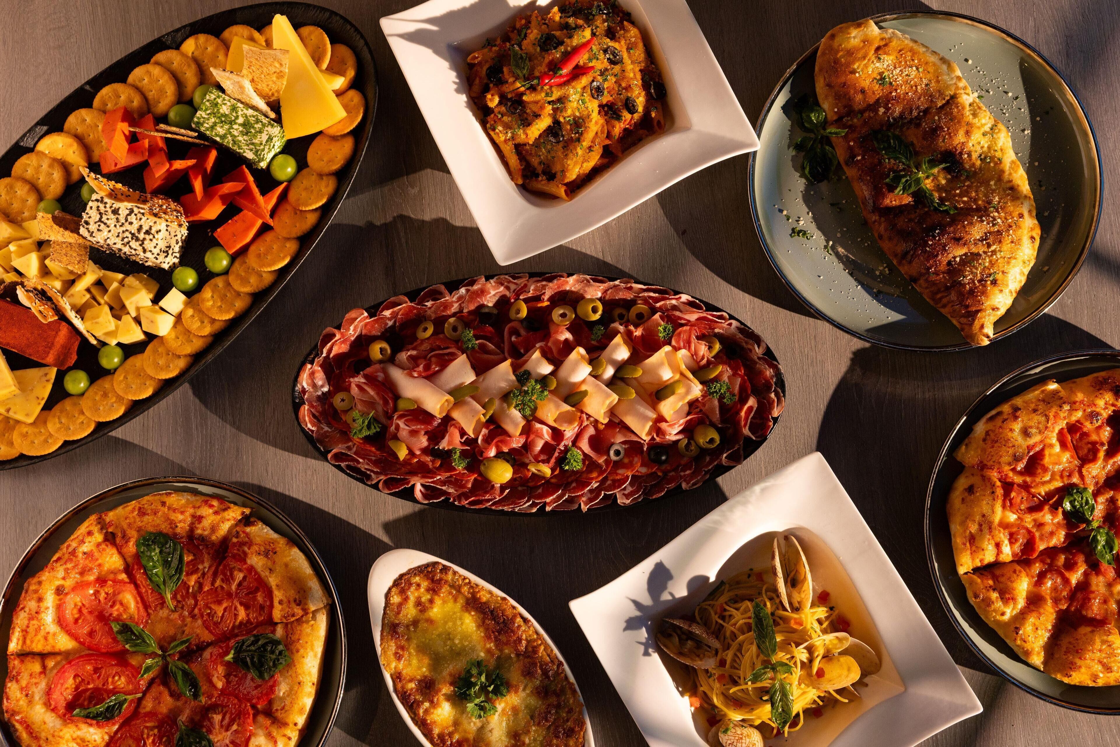 A variety of dishes including pizza, a charcuterie board, and a baked dish, arranged on a table.