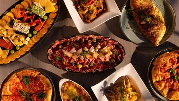 A variety of dishes including pizza, a charcuterie board, and a baked dish, arranged on a table.