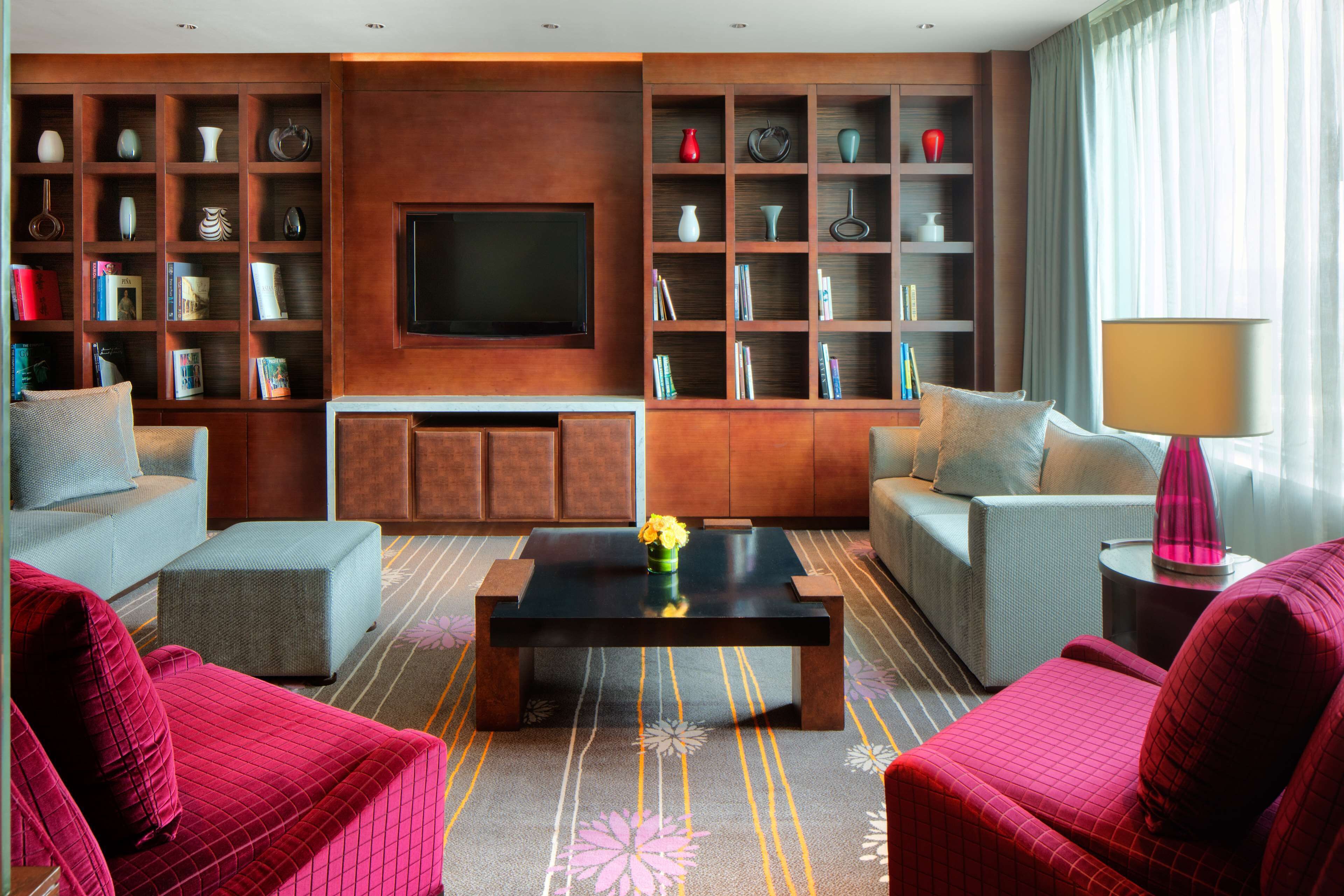 A modern living room with a flat-screen TV, a coffee table with a vase, and a bookshelf filled with books and decorative items.