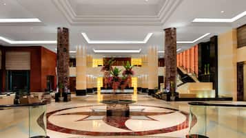 A spacious lobby with a central decorative fountain, a marble floor, and a staircase leading to upper levels.