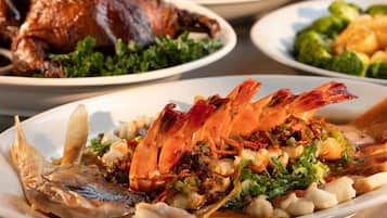 A variety of seafood dishes including a whole cooked fish, shrimp, and a roasted duck on a table.
