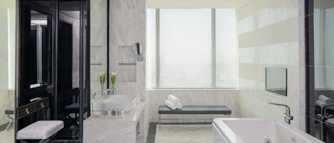 Un baño moderno con una bañera grande, una banca, un tocador con espejo y un ventanal que proporciona luz natural.