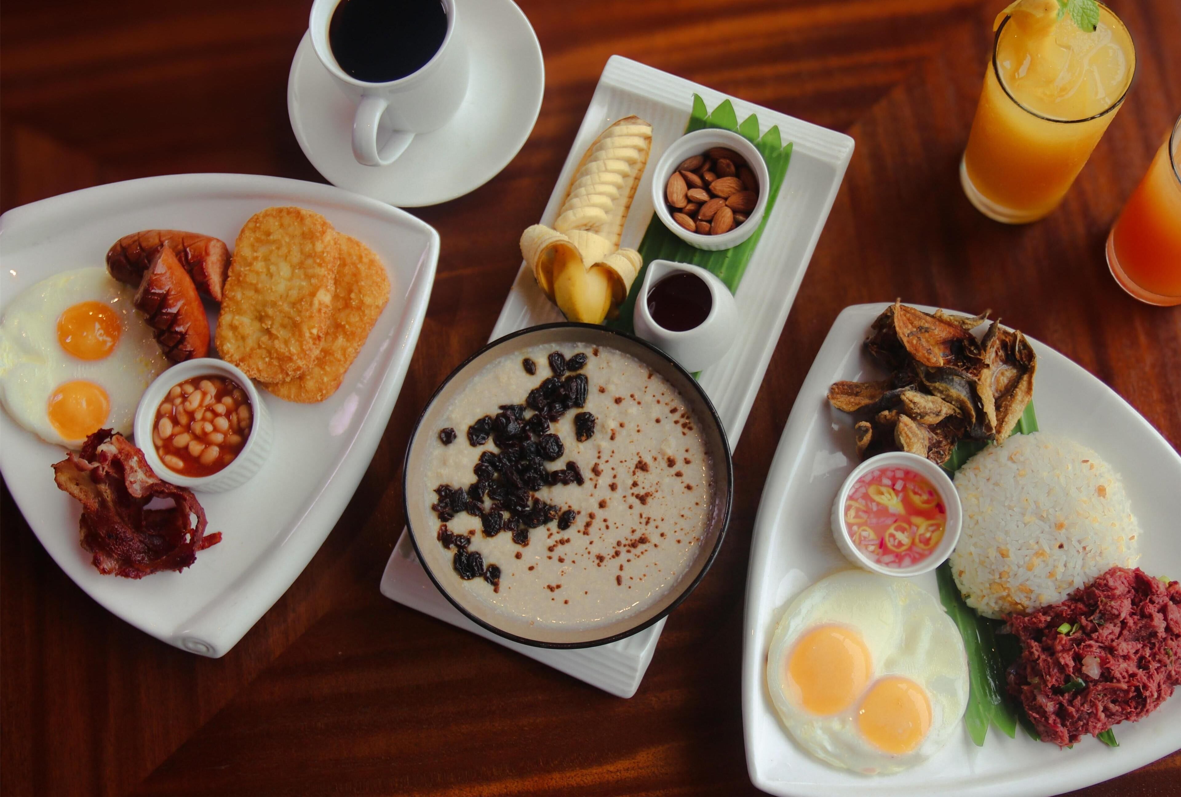 A breakfast spread with eggs, bacon, toast, beans, a bowl of porridge, a banana, almonds, and a glass of orange juice.
