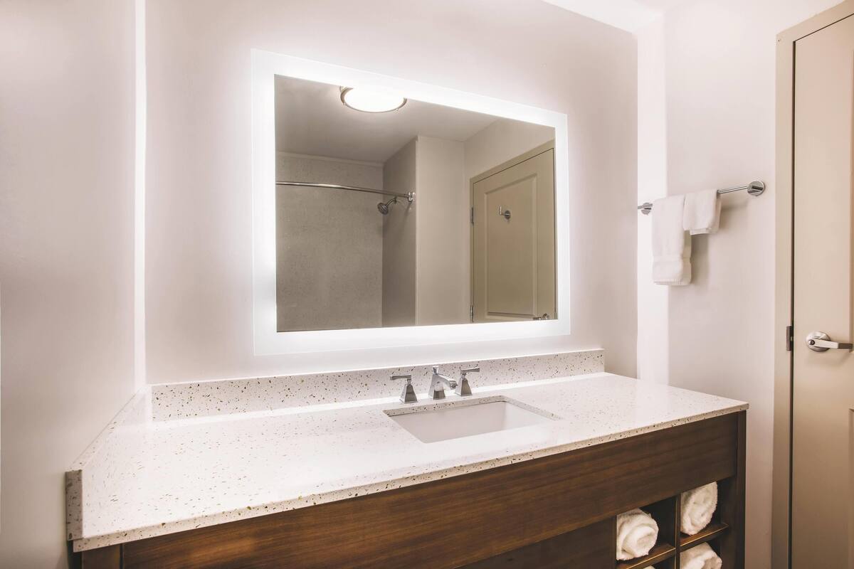 Une salle de bain avec un comptoir blanc à motifs, un miroir rectangulaire, un espace douche et un porte-serviettes.