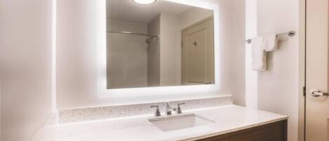 A bathroom with a white speckled countertop, a rectangular mirror, a shower area, and a towel rack.