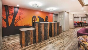Un área de recepción con un mostrador de madera, un mural de árboles y un atardecer, y una sala de conferencias al fondo.