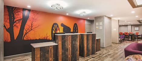 A reception area with a wooden reception desk, a mural of trees and a sunset, and a conference room in the background.