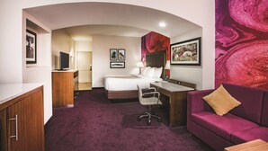 Habitación de hotel con cama, escritorio, silla y sofá morado.