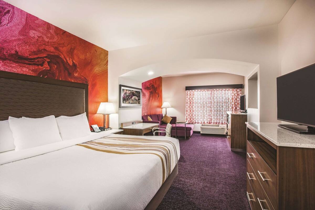 Une chambre d’hôtel avec un grand lit, un bureau, une chaise, une télévision et une fenêtre avec des rideaux.