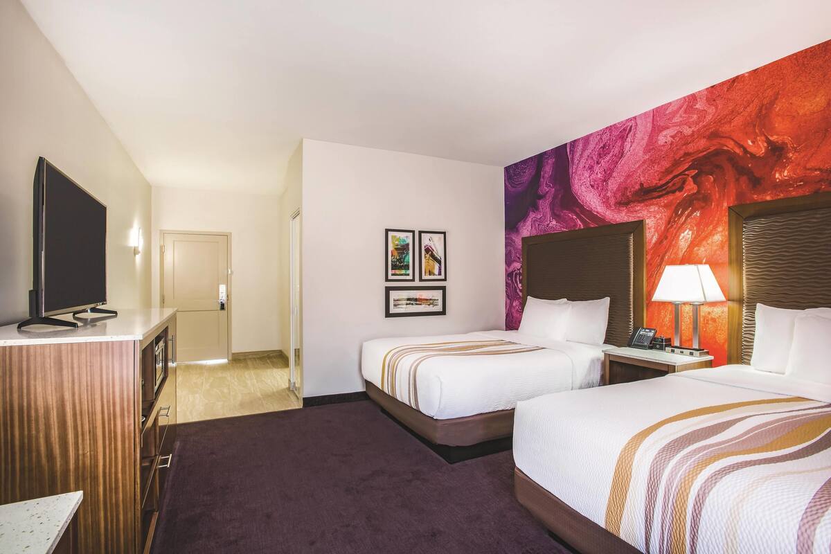 Une chambre d’hôtel avec deux lits, une télévision, un bureau et un mur décoré d’œuvres d’art.