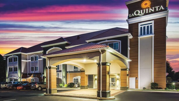 Un hotel con un letrero llamativo, un acceso cubierto y un estacionamiento.
