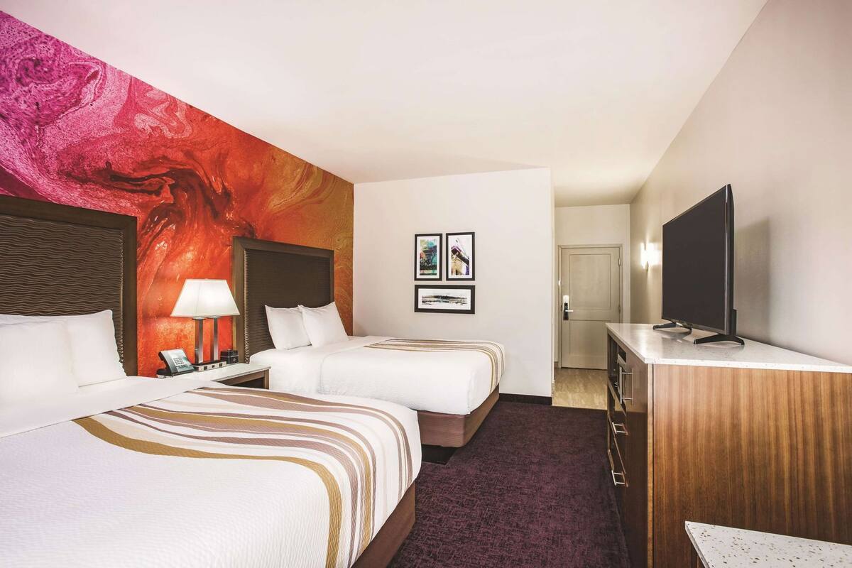 Une chambre d’hôtel avec deux lits, une télévision, un bureau et un mur décoré d’œuvres d’art.
