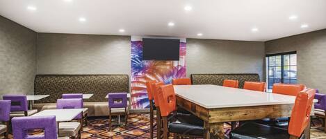 A conference room with a large table, multiple chairs, a sofa, and a TV screen.