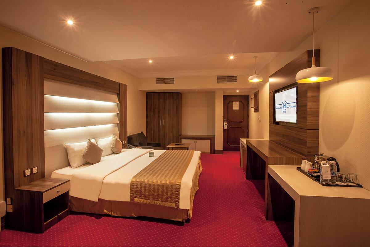 A hotel room with a large bed, a desk, a TV, and a red carpet.