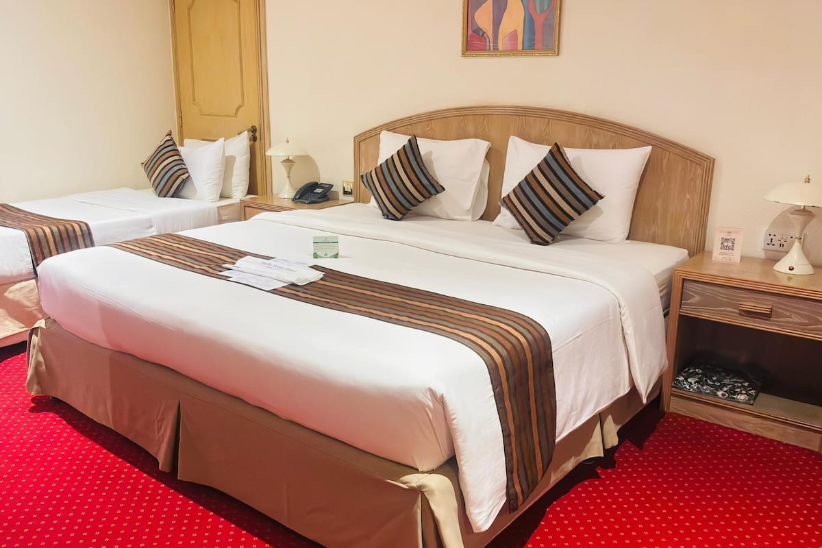 A hotel room with two beds, a red carpet, a wooden headboard, a nightstand with a lamp, and a painting on the wall.