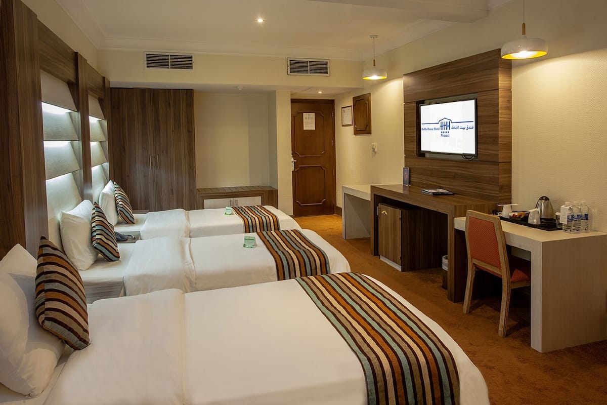A hotel room with two beds, a desk, a chair, and a television.