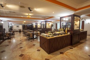 A spacious dining area with multiple tables and chairs, a central buffet counter, and a polished marble floor.
