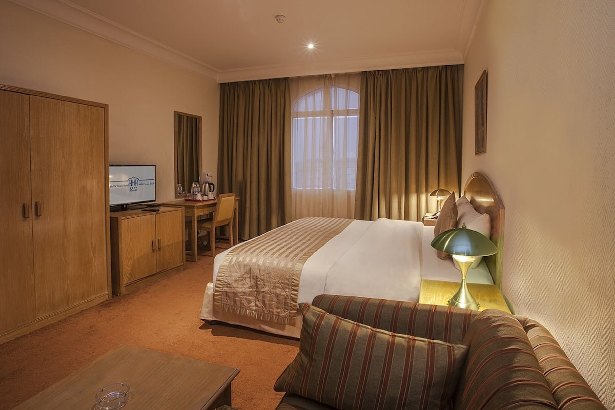 A hotel room with a bed, a desk, a television, a sofa, and a window with curtains.