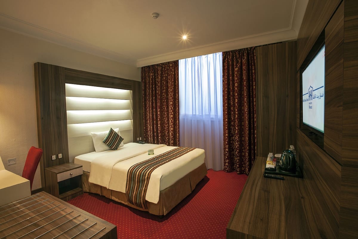 A hotel room with a large bed, a desk, a TV, and a window with curtains.