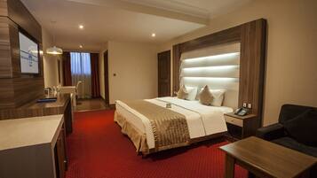 Ein Hotelzimmer mit einem großen Bett, einem Schreibtisch, einem Stuhl und einem Fernseher an der Wand.