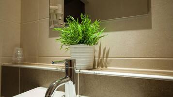 Un baño con lavamanos blanco, grifo cromado, una planta en maceta y un espejo sobre el lavamanos.