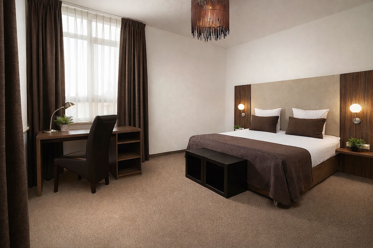 Quarto de hotel com cama, escrivaninha, cadeira e luminária suspensa.