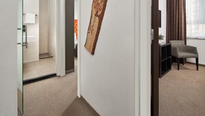 A hallway with a wooden wall art piece, a chair, and a TV on a stand. - Hotel La Reine (Eindhoven)