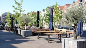 An outdoor seating area with tables and chairs, surrounded by trees and buildings. - Hotel La Reine (Eindhoven)