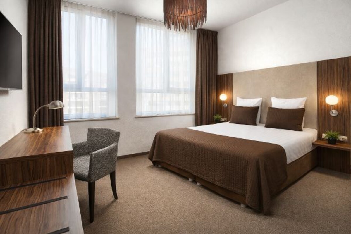 A hotel room with a large bed, a desk, a chair, a TV, and two bedside lamps.