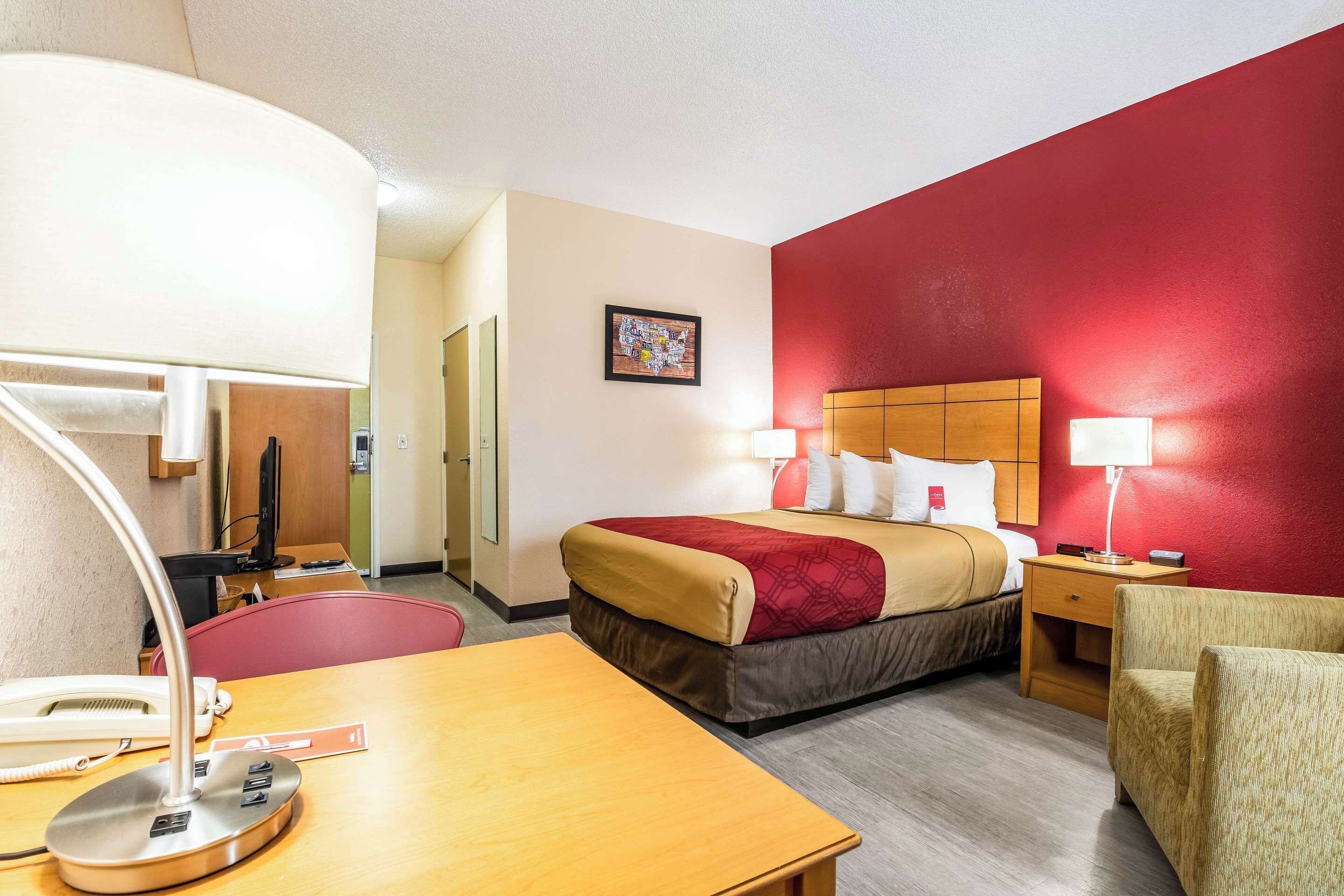 A hotel room with a bed, bedside tables, a desk with a lamp, a chair, and a telephone.