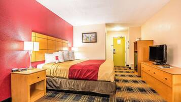 A hotel room with a bed, bedside table, lamp, TV, and a door leading to another room.