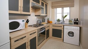 A compact kitchen with a microwave, stove, oven, and washing machine. - Your Stay Bristol Orchard Gate (Bristol)