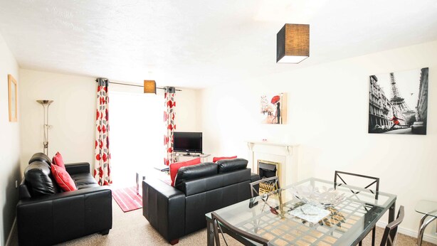 A living room with a black sofa, a glass coffee table, and a fireplace. - Your Stay Bristol Orchard Gate (Bristol)