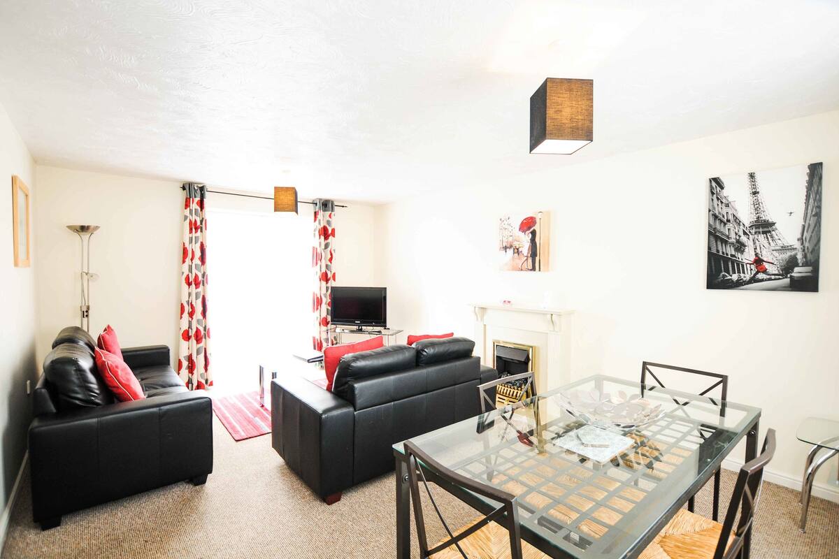 A living room with a black sofa, a glass coffee table, and a fireplace.